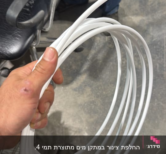 יד מחזיקה צינור לבן מגולגל על רקע רצפה אפורה